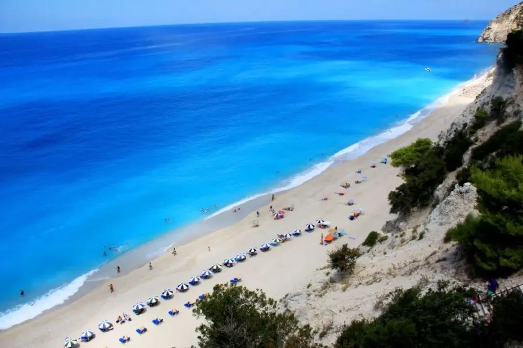 Egremni Beach on Lefkada Island, Greece, a long stretch of white sand and pebbles bordered by turquoise Ionian Sea waters and dramatic limestone cliffs.
