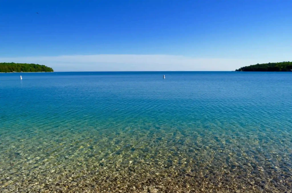 Schoolhouse Beach on Washington Island, Wisconsin, a unique shoreline covered in smooth limestone pebbles, bordered by clear turquoise water and surrounded by forested landscape.