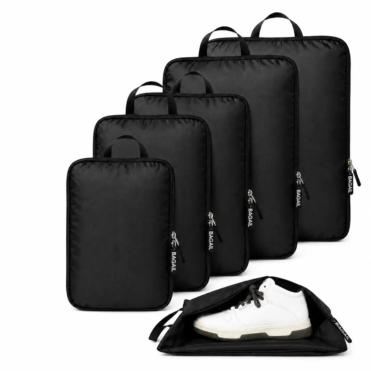 Five black packing cubes of varying sizes are neatly arranged in a row, with one lying open in front displaying a pair of white sneakers inside. Each cube has a zipper and a carrying handle.