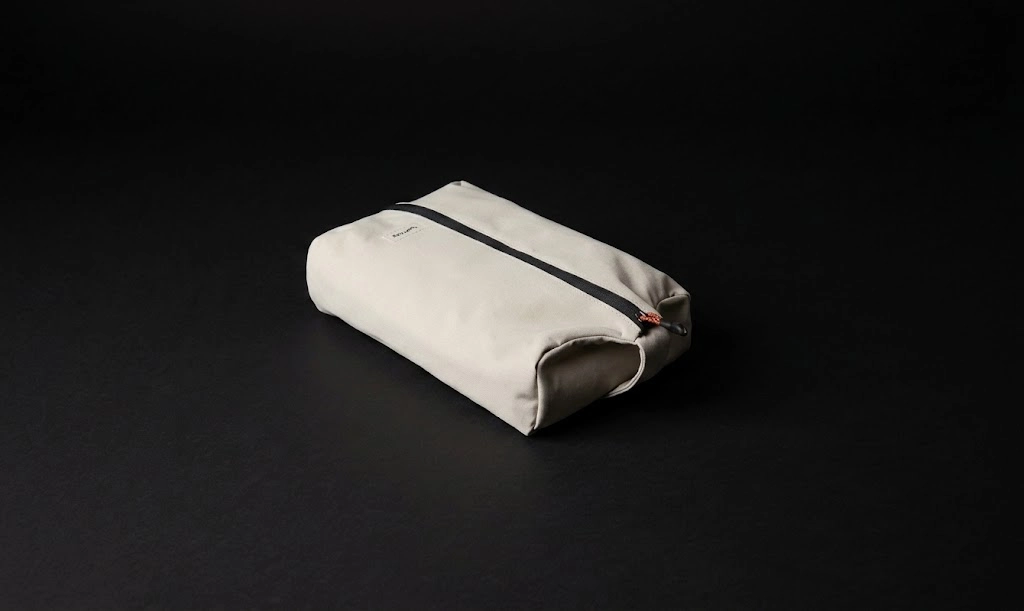 A beige rectangular zippered pouch sits on a black background, closed and viewed at an angle to show its simple, minimalist design.